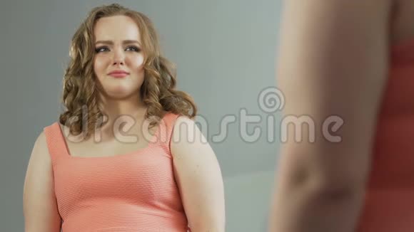 一个体重超标的女孩看着镜子的倒影痛苦地哭着视频的预览图