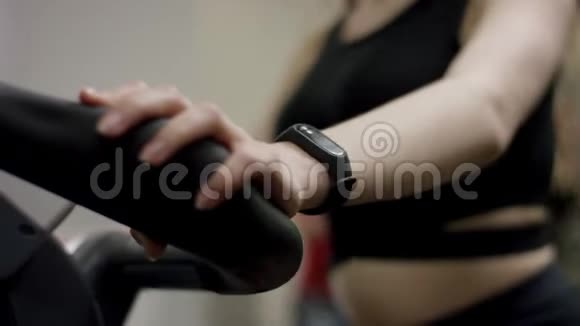 穿着黑色运动的可爱女孩几乎不穿运动自行车在新的健身房里专注于双手视频的预览图