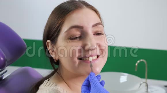 牙齿颜色样本的牙医正在牙科诊所为女性患者的牙齿选择阴影视频的预览图
