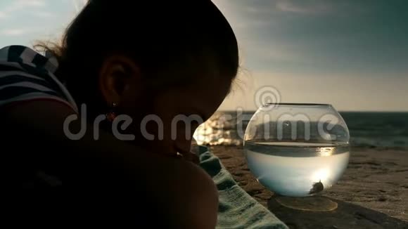 小女孩躺在海滩上看着夕阳下鱼缸里的小鱼视频的预览图