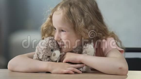 快乐的孩子坐在桌边抱着泰迪熊微笑着童年视频的预览图
