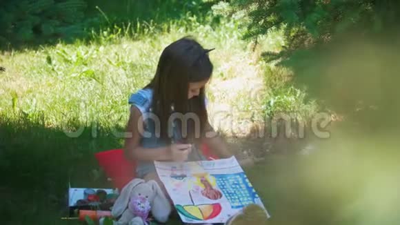 快乐的小女孩在晴天坐在草地上画水彩画视频的预览图