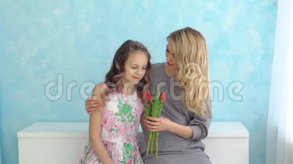 母亲和女儿带着一束郁金香坐在蓝色的墙壁背景上视频的预览图