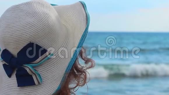 带帽子的悲伤年轻女子独自坐在沙滩上望着海浪视频的预览图