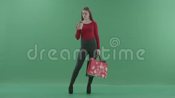 穿着休闲服的漂亮女人正拿着购物袋喝着咖啡或茶她站在工作室里视频的预览图