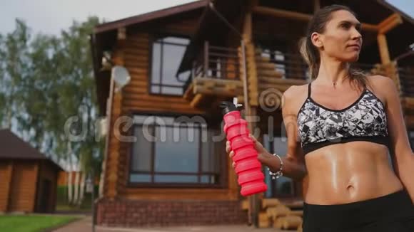 棕色皮肤的黑发女人肌肉膨胀穿着黑色短裤在街上锻炼身体后喝蛋白质视频的预览图