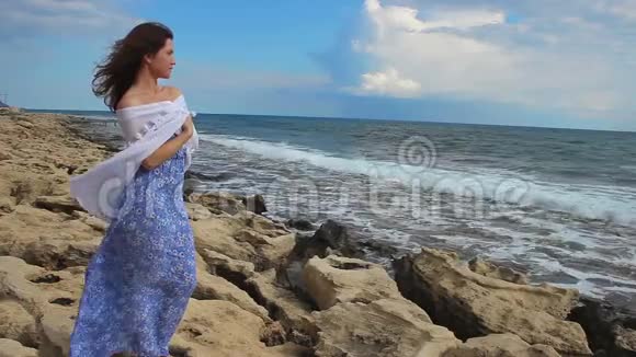 悲伤孤独的年轻女子望着暴风雨的大海海浪飞溅岩石的海岸风视频的预览图
