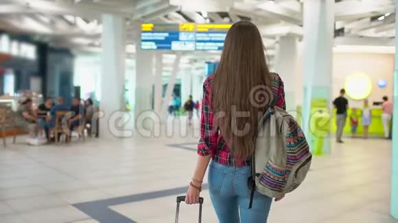 年轻的旅行女性穿着休闲衬衫带着行李在现代机场航站楼里行走从后面看城市视频的预览图