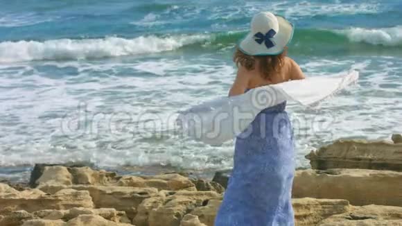 穿着长裙的迷人女人在岩石海岸看海浪的慢动作视频的预览图
