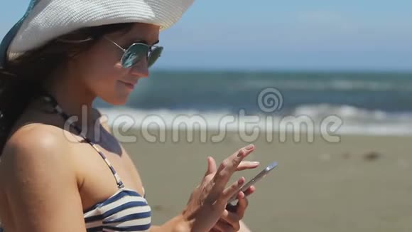 漂亮快乐的女人在智能手机上发短信暴风雨般的大海沙滩背景视频的预览图