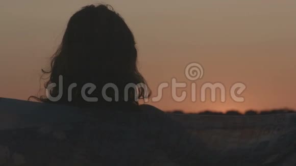 孤独的女人看着日出日落时燃烧的天空头发随风飘动视频的预览图