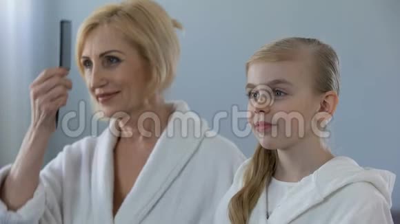 成熟的女性和孙女梳头对着镜子微笑视频的预览图