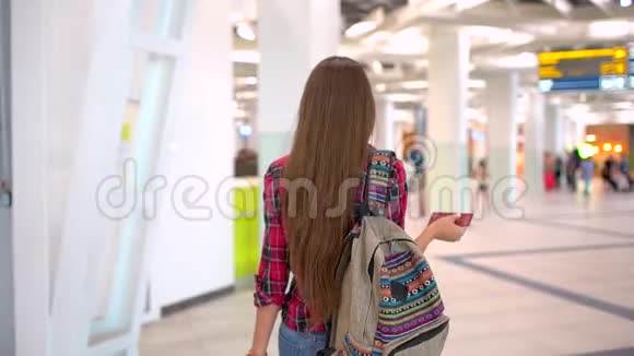 年轻的旅行女性穿着休闲衬衫带着行李在现代机场航站楼里行走从后面看城市视频的预览图