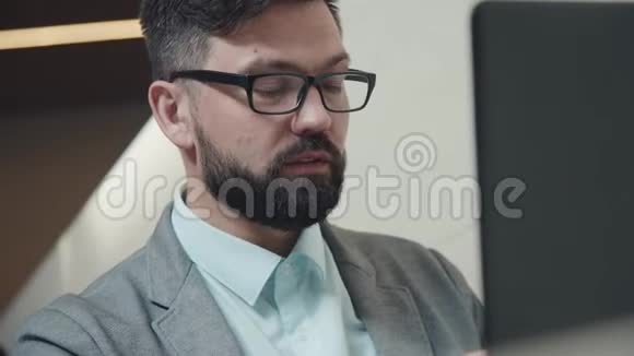 野心勃勃的男人长着闪光和胡须他坐在笔记本电脑前视频的预览图