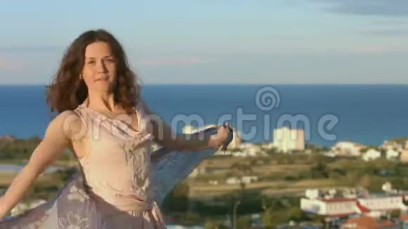 美丽的幸福女人带着围巾跳舞背景中的海洋景观令人惊叹视频的预览图