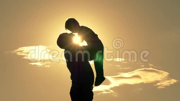 幸福的父亲的剪影牵着他的手在夕阳的背景下亲吻他的孩子幸福的概念视频的预览图