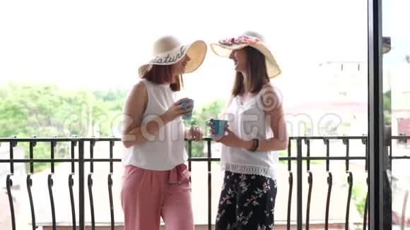 两个戴着大夏帽的漂亮年轻女人在阳台上喝着咖啡和聊天视频的预览图
