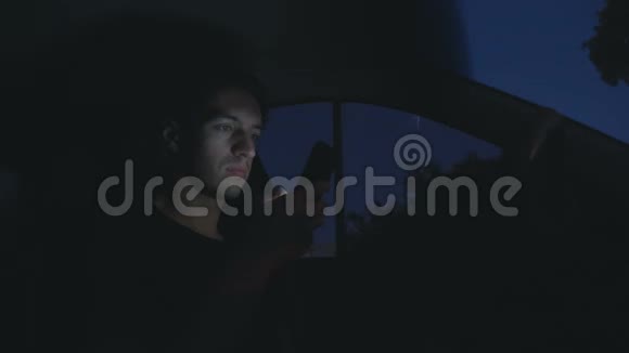 一个年轻人在夜间坐在马路上的车里用智能手机视频的预览图
