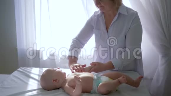 女治疗师在沙龙窗口附近的桌子上按摩新生儿的手视频的预览图