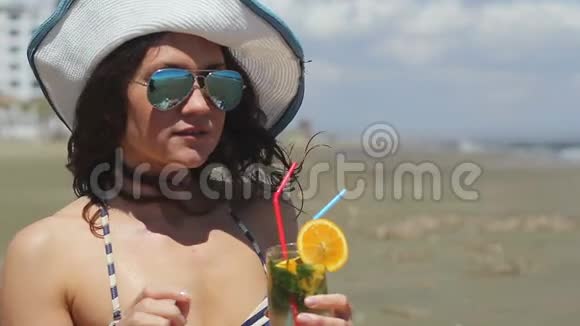 戴着墨镜和帽子的贴身美女在海滩上喝了很久视频的预览图