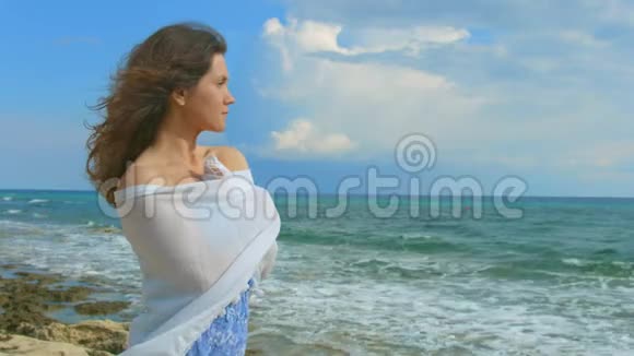 孤独的黑发女人裹着围巾看着海浪风天气视频的预览图