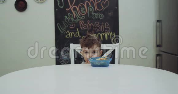 小男孩坐在厨房的椅子上拿着一根棒棒糖高兴地躲在盘子后面4k视频的预览图