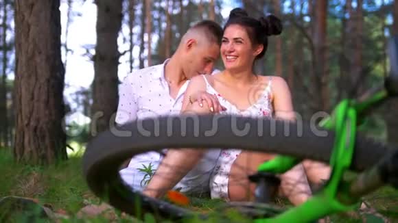一辆自行车的车轮躺在草地上幸福的恋人在夏天的森林里骑自行车后休息视频的预览图
