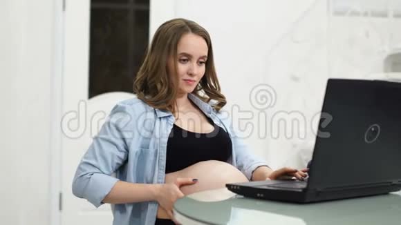 孕妇作家在休产假时坐在电脑前抚摸着一本新书的几页视频的预览图