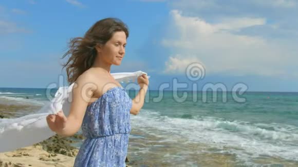 快乐微笑的黑发女人在风中挽着白色的围巾海滨阳光明媚视频的预览图