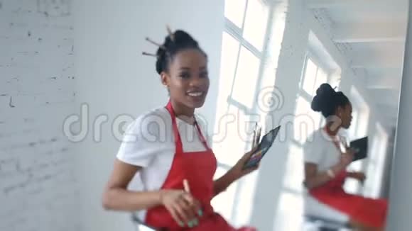 积极微笑的非洲美容师拿着刷子在巨大镜子旁边的椅子上旋转视频的预览图