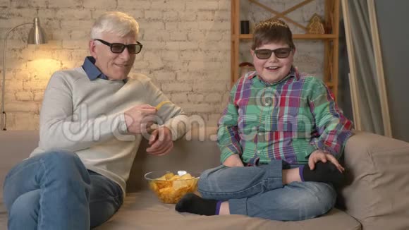 祖父正用手中的薯片喂他的孙子一位老人和一个年轻的胖男孩坐在上面视频的预览图