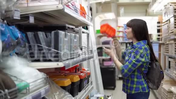 一个年轻的女人在一家建筑超市里选择了一个小橙色的容器视频的预览图
