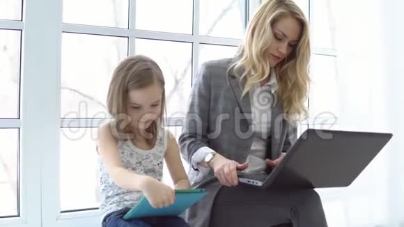 年轻的商务女性手提电脑和小女孩坐在窗边视频的预览图