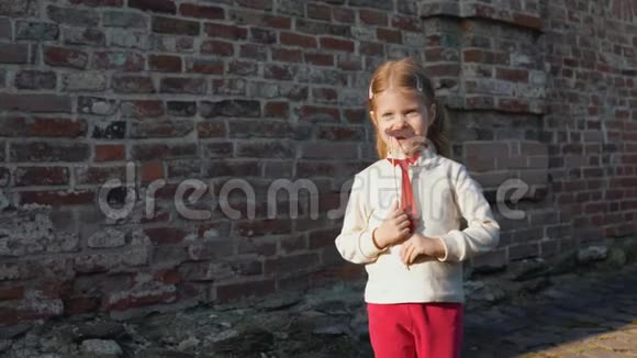 小女孩拿着一根纸胡子在棍子上站在砖墙旁边视频的预览图