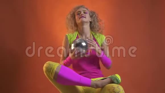 身着80年代服装的金发女郎端坐着玩迪斯科舞厅橙色背景视频的预览图