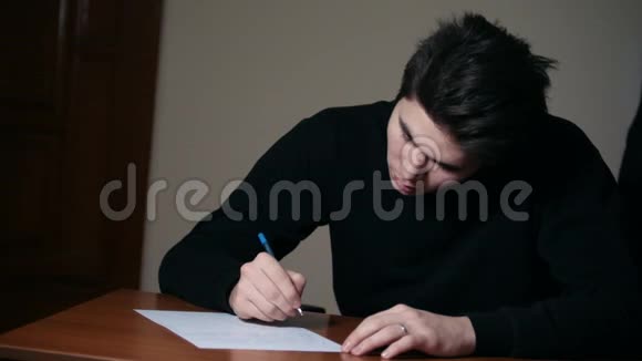 一个黑发男子在黑暗的房间里用笔在纸上写文字视频的预览图