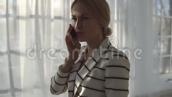 年轻的金发女人在一扇大窗户旁边打电话视频的预览图