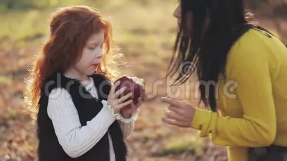 一位快乐的母亲和可爱的小女儿坐在一起在城市公园野餐时玩苹果秋季时间视频的预览图