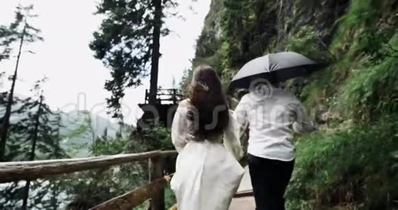 年轻夫妇在浪漫的旅行中从木桥上奔跑在壮丽的风景和大山中间视频的预览图