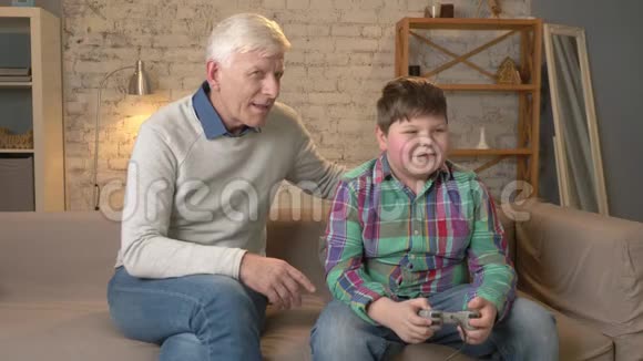 爷爷看着孙子玩游戏机老人正和一个小胖子坐在沙发上视频的预览图