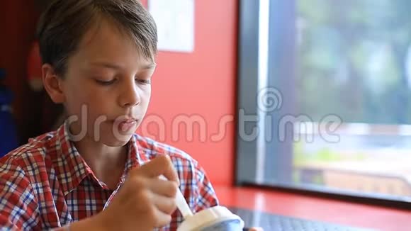 一个男孩正在咖啡馆里吃冰淇淋咖啡馆里那个金发男孩正在用勺子吃冰淇淋视频的预览图