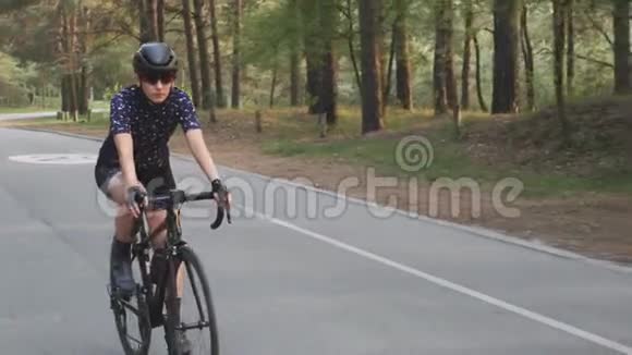 骑着黑色自行车的女孩穿着蓝色球衣和黑色头盔在公园里骑马自行车比赛的训练慢动作视频的预览图