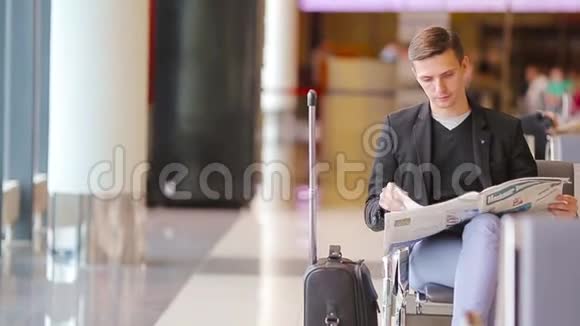 年轻的白种人在机场等待登机时带着报纸穿西装的休闲青年商人视频的预览图
