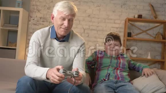 爷爷和孙子坐在沙发上玩游戏机一位老人坐在沙发上视频的预览图