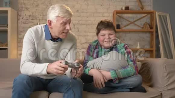 爷爷和孙子坐在沙发上玩游戏机一位老人坐在沙发上视频的预览图