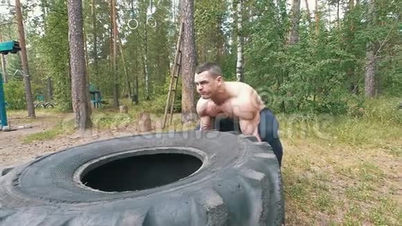 强壮的肌肉男举起一个巨大的橡胶轮在森林里锻炼视频的预览图