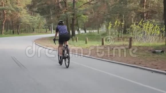 年轻的健康女孩骑自行车在公园里戴着黑色头盔蓝色球衣和眼镜慢动作视频的预览图