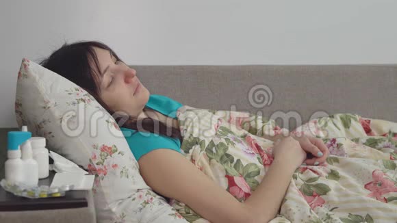 感冒的年轻女人坐在毯子里的床上视频的预览图