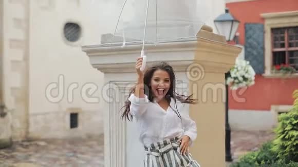 快乐的年轻女子在老城的街道上用雨伞跳舞和玩漂亮的卷发造型视频的预览图