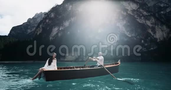 浪漫的情侣在湖中央的木船上做特写男人正在划船他的女朋友在玩腿视频的预览图
